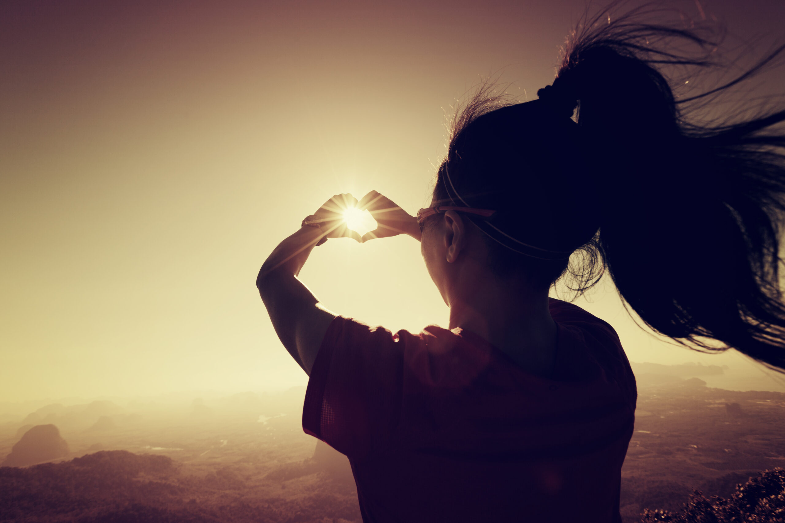 Woman Making a Heart Shape Over Sunrise